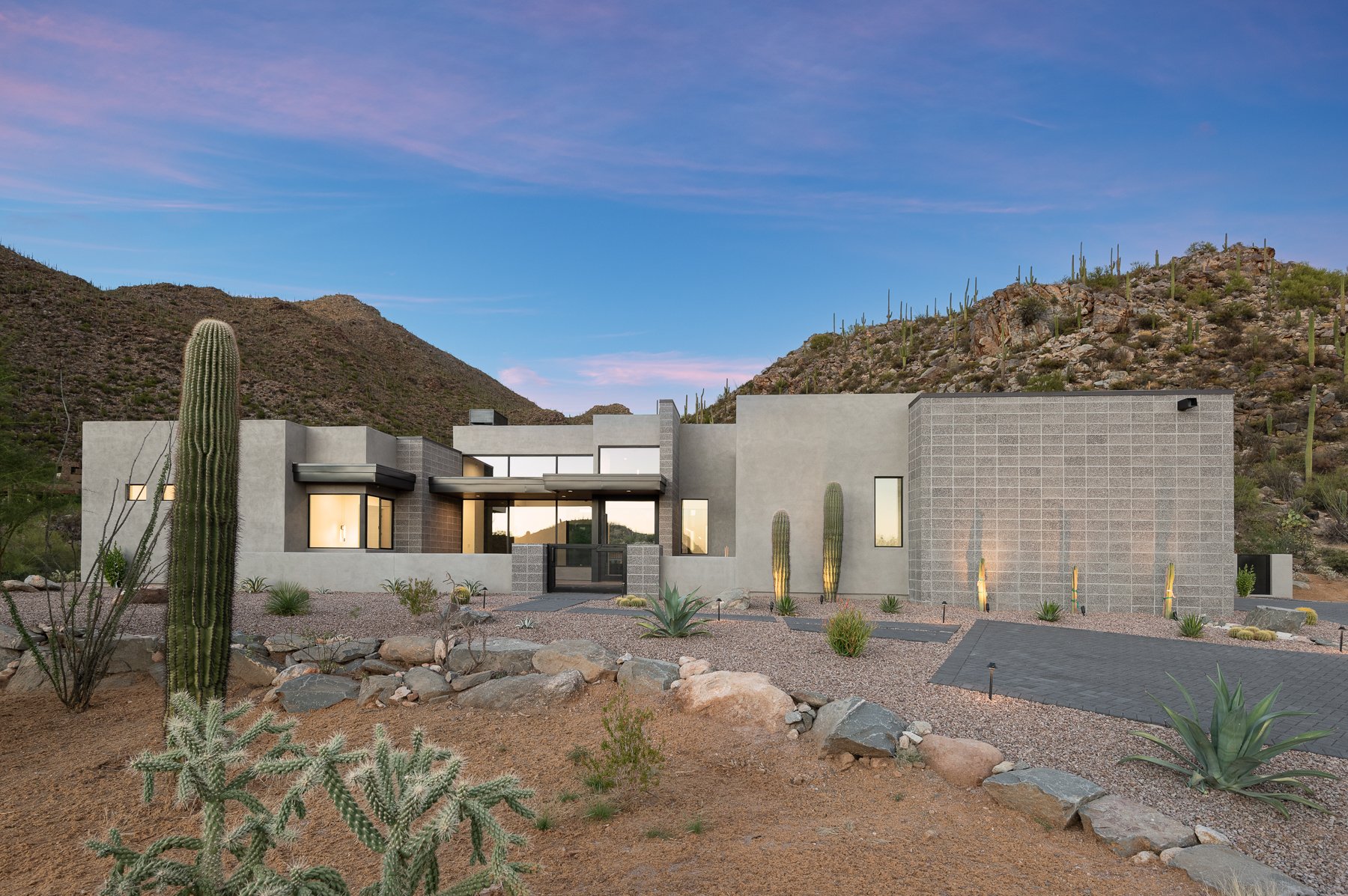 Modern desert home with cacti, mountainous landscape, and sunset sky background.