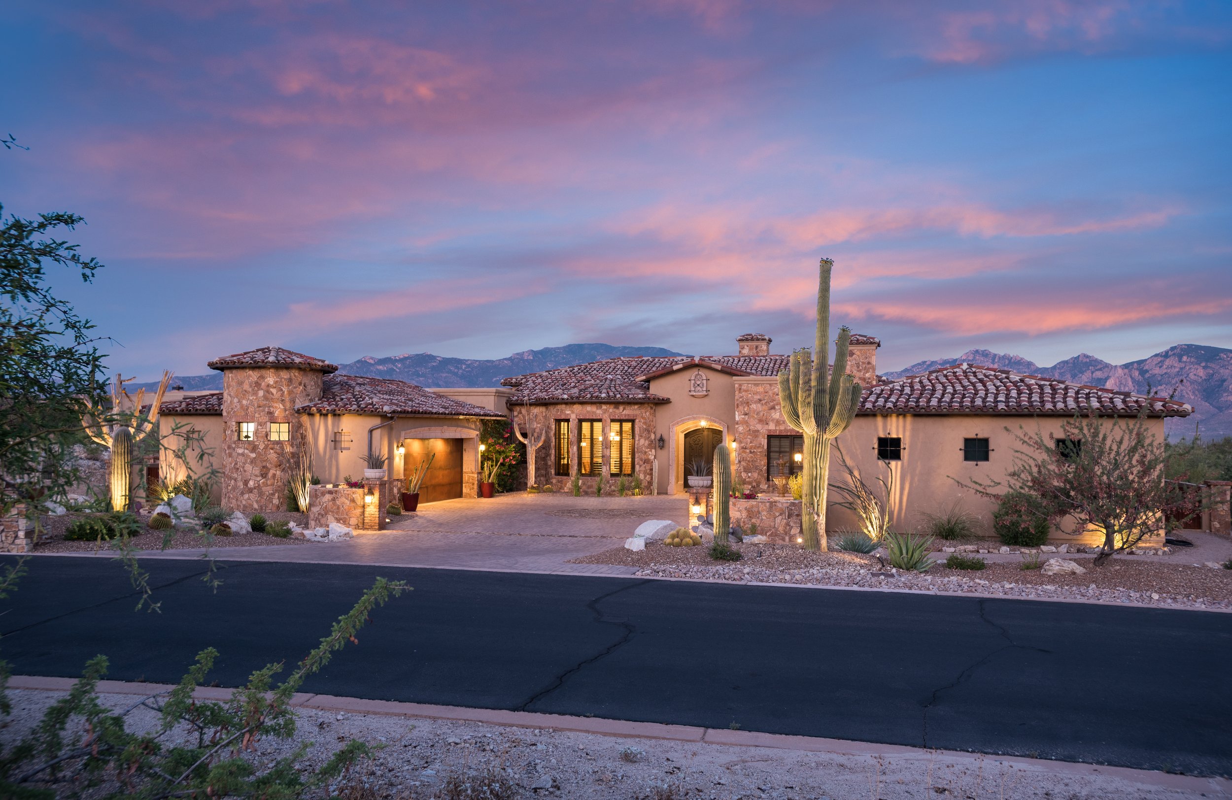 Luxury desert home at sunset with stone facade, tile roof, and cacti landscaping.